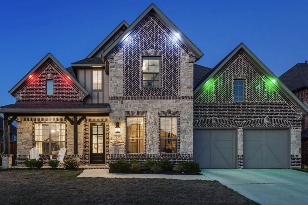 Warm soffit downlighting washing light down a stone home facade at night