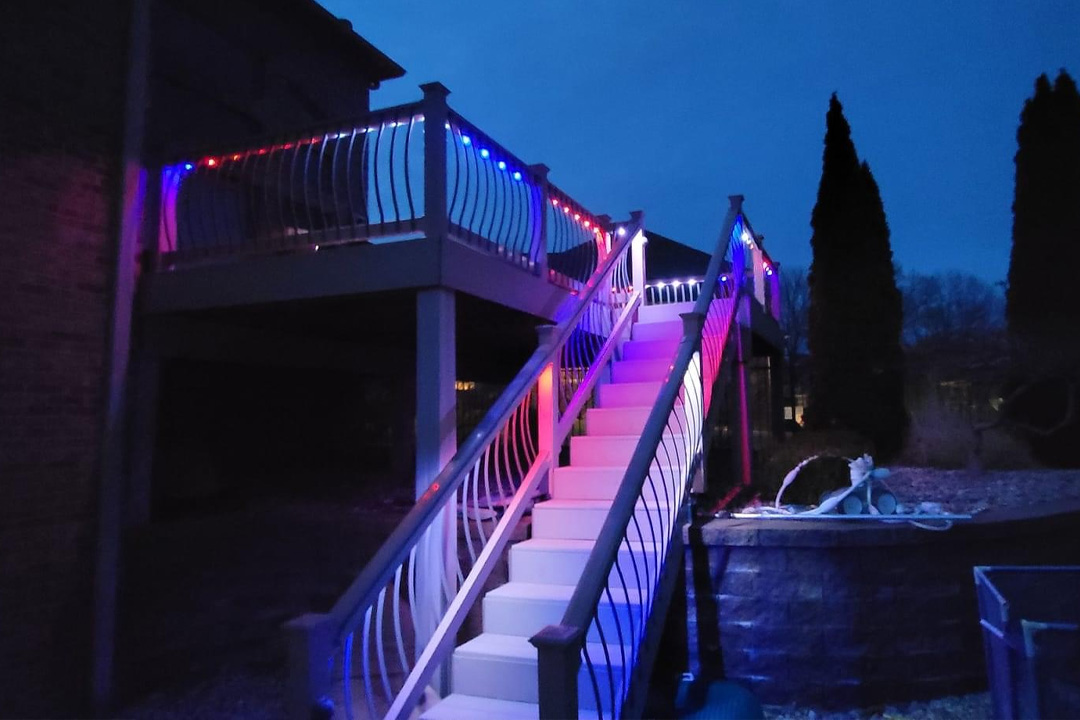 Backyard patio lit by warm globe string lights and landscape uplighting